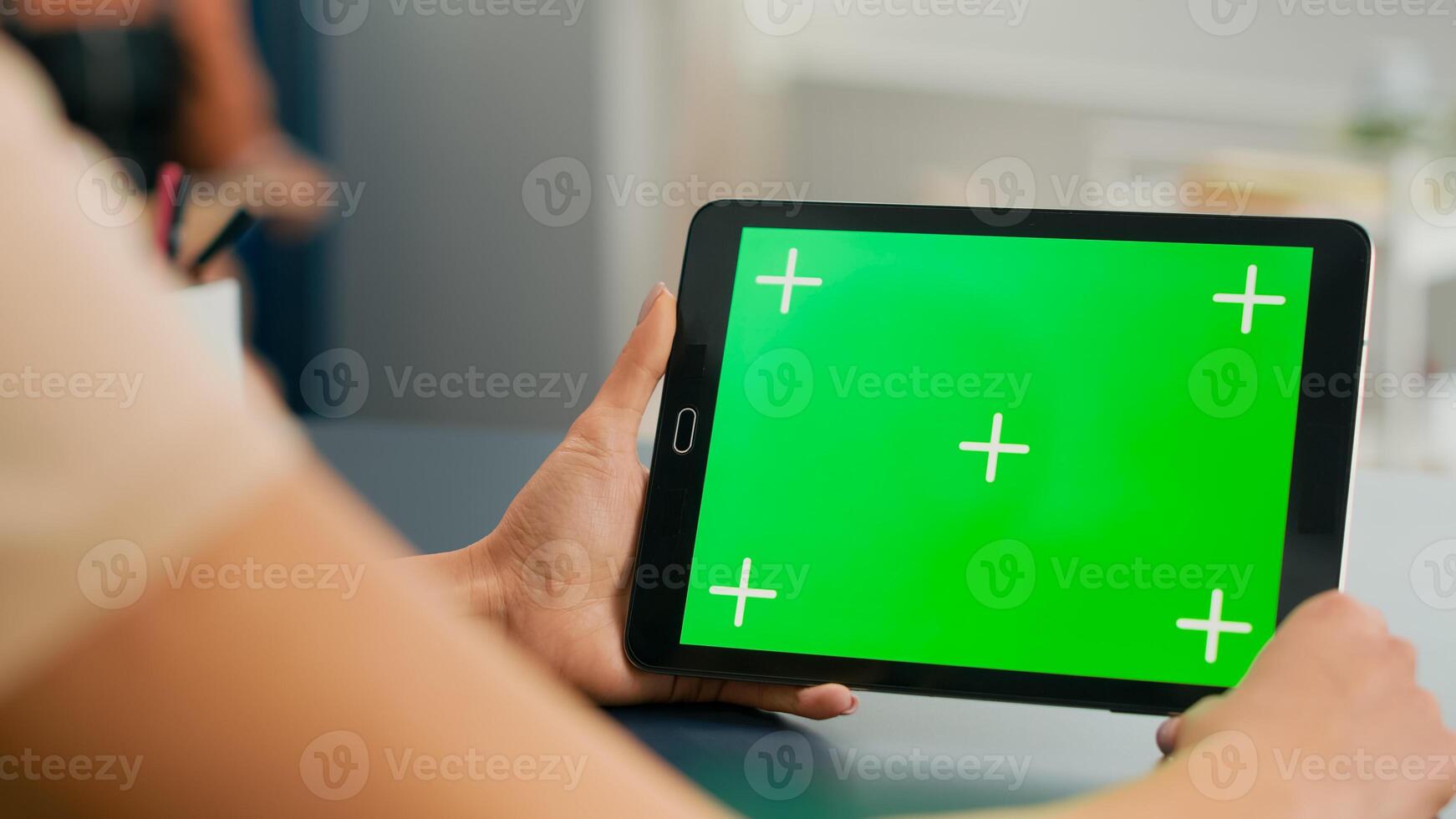 Tablet computer with mock up green screen chroma key display standing on table desk. Freelancer woman browsing on isolated device for online web communication in home office room photo
