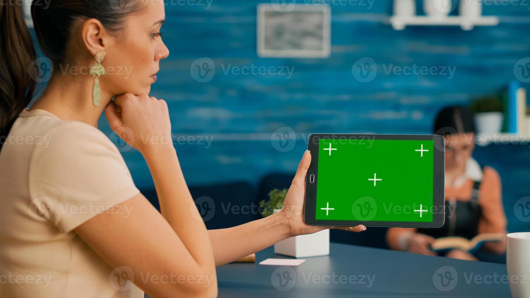 Back view of woman holding tablet computer with mock up green screen chroma key display. Caucasian female using touchscreen device for online browsing sitting in home office studio photo