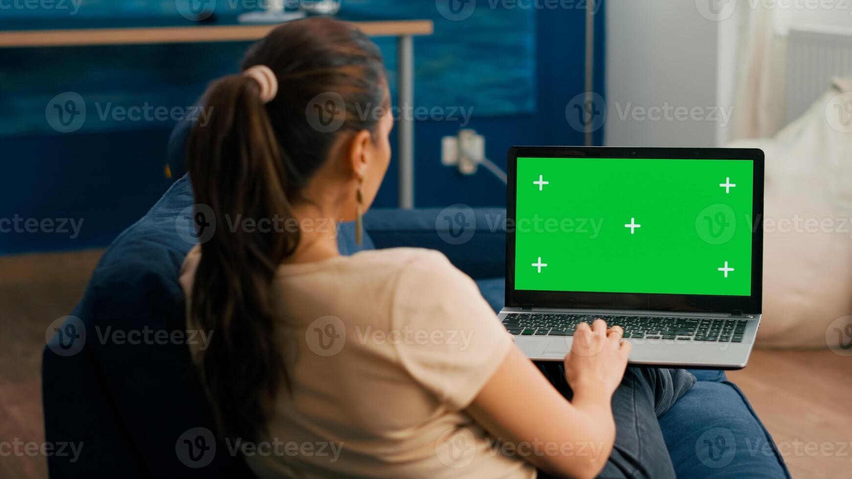 Freelancer woman sitting on sofa in home office typing on laptop computer with mock up green screen chroma key display. Caucasian woman working on financial graphs using isolated pc photo
