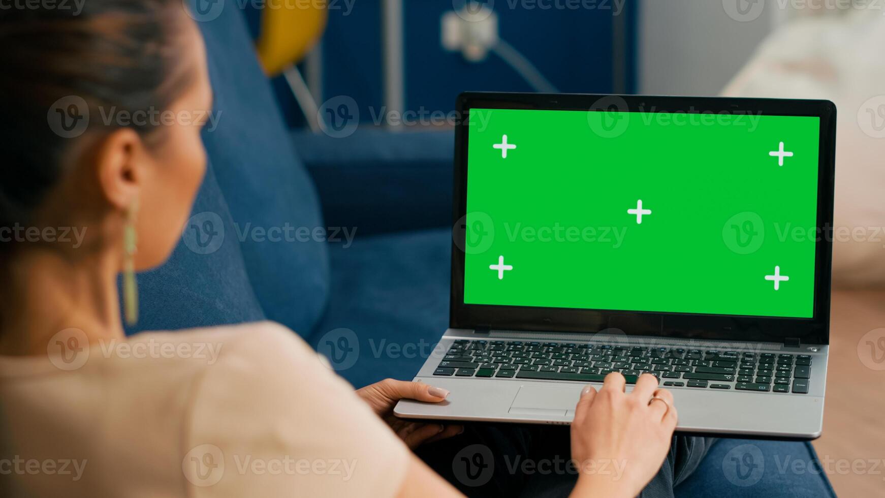 Woman sitting on couch in cozy living room working on laptop computer with mock up green screen chroma key display. Freelancer using isolated pc, browsing on internet for social media advertising photo