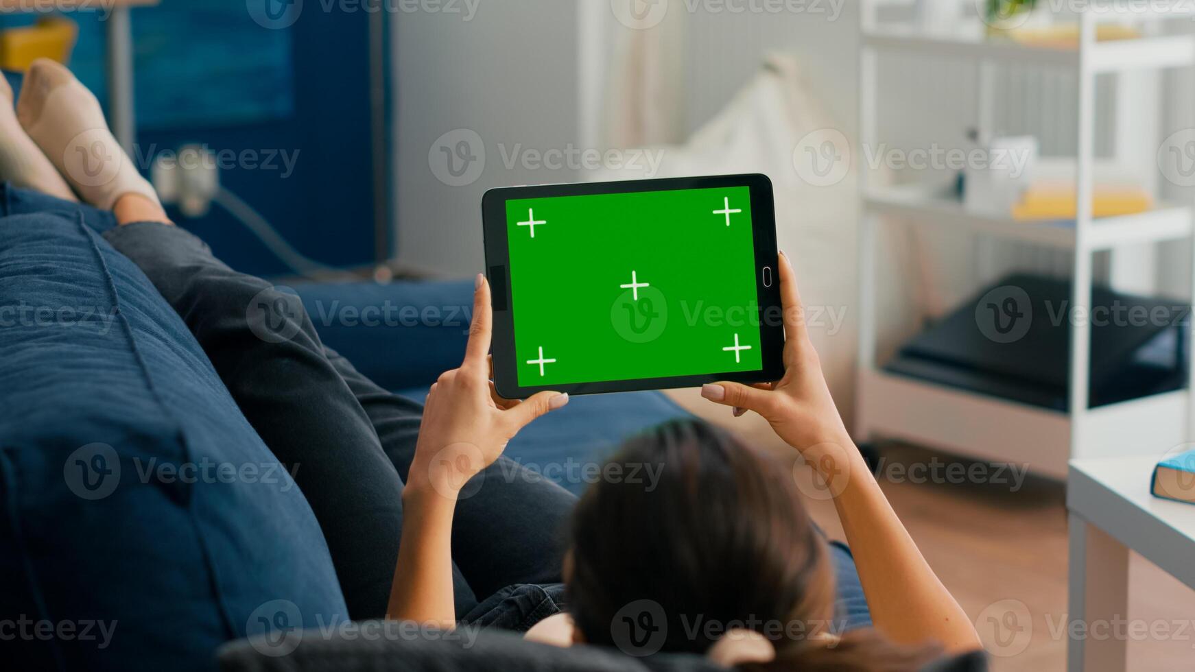 Woman sitting on sofa in living room watching movies on tablet computer with mock up green screen chroma key display. Freelancer using isolated touchscreen device for social networks browsing photo