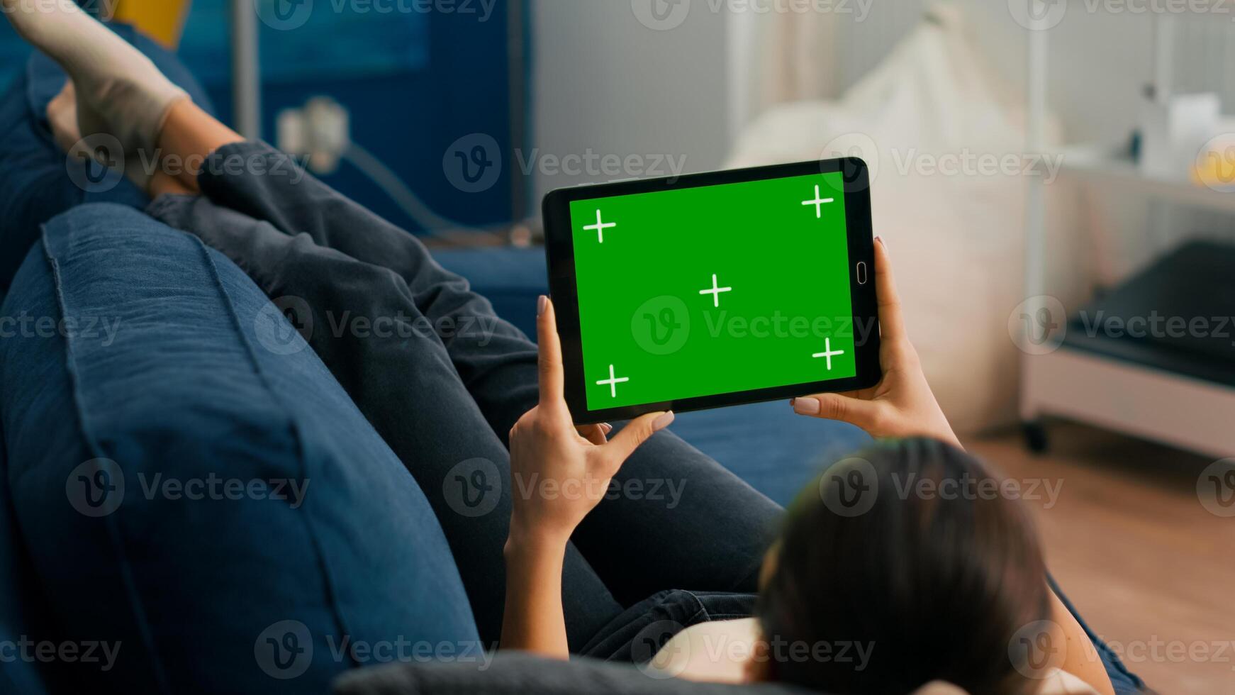 Close up of woman looking at tablet computer in horizontal mode with mock up green screen chroma key display lying on couch. Freelancer using isolated touchscreen device for social networks browsing photo