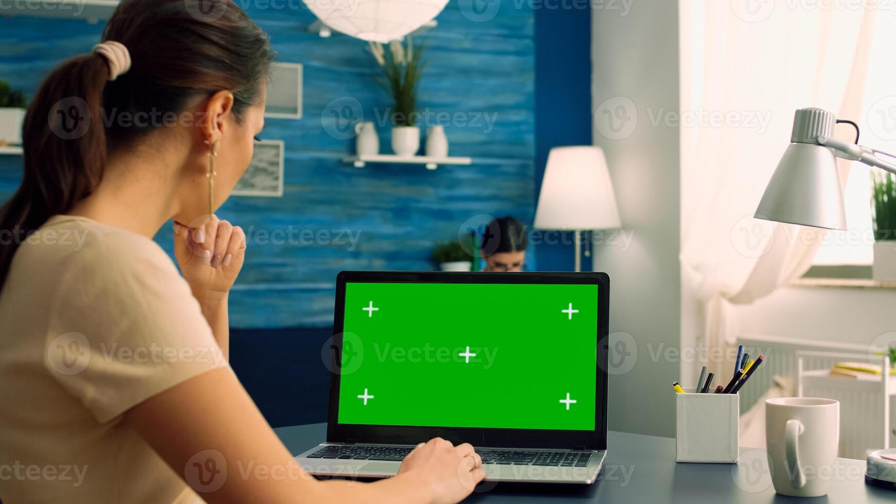 Freelancer looking at laptop computer with mock up green screen chroma key display sitting on desk table in office home. Business woman typing ideas for business commerce using isolated pc photo