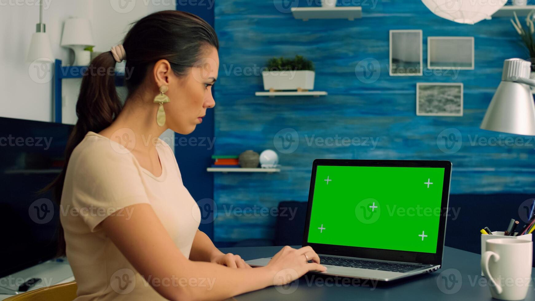 Caucasian female typing on laptop computer with mock up green screen chroma key display for online communication sitting on desk table. Freelancer working with isolated pc in home office studio photo