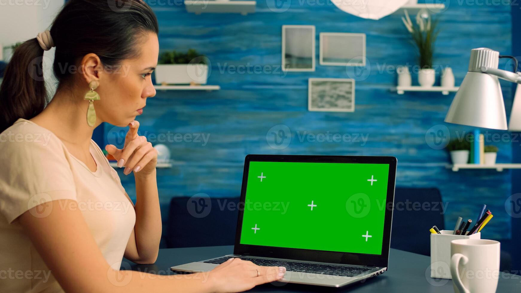 Caucasian female working at business comunication project on laptop computer with mock up green screen chroma key display. Freelancer sitting on desk in home office studio equipped with isolated pc photo