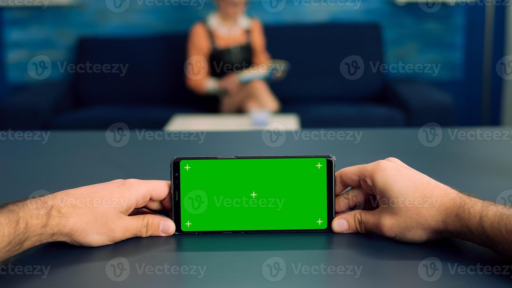 Pov of man hands holding in horizontal mode smartphone with mock up green screen chroma key display standing on desk in office studio. Freelancer using isolated phone for browsing social networks photo