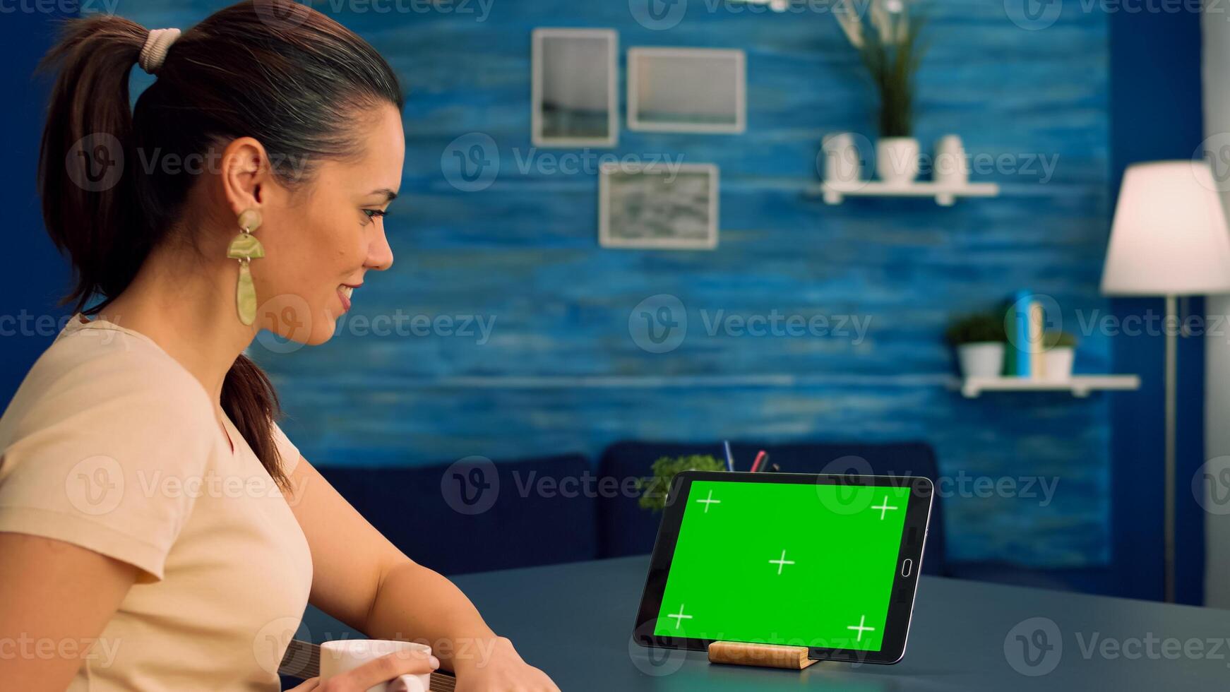 Freelancer holding touchpad with mock up green screen standing on office desk in living room. Woman looking at template chroma key isolated tablet computer display using technology internet photo