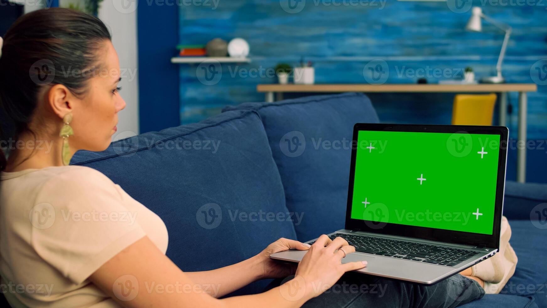 Tracking shot of freelencer woman typing on mock up green screen chroma key laptop computer for marketing ideas. Caucasian female lying on sofa in living room using isolated pc photo