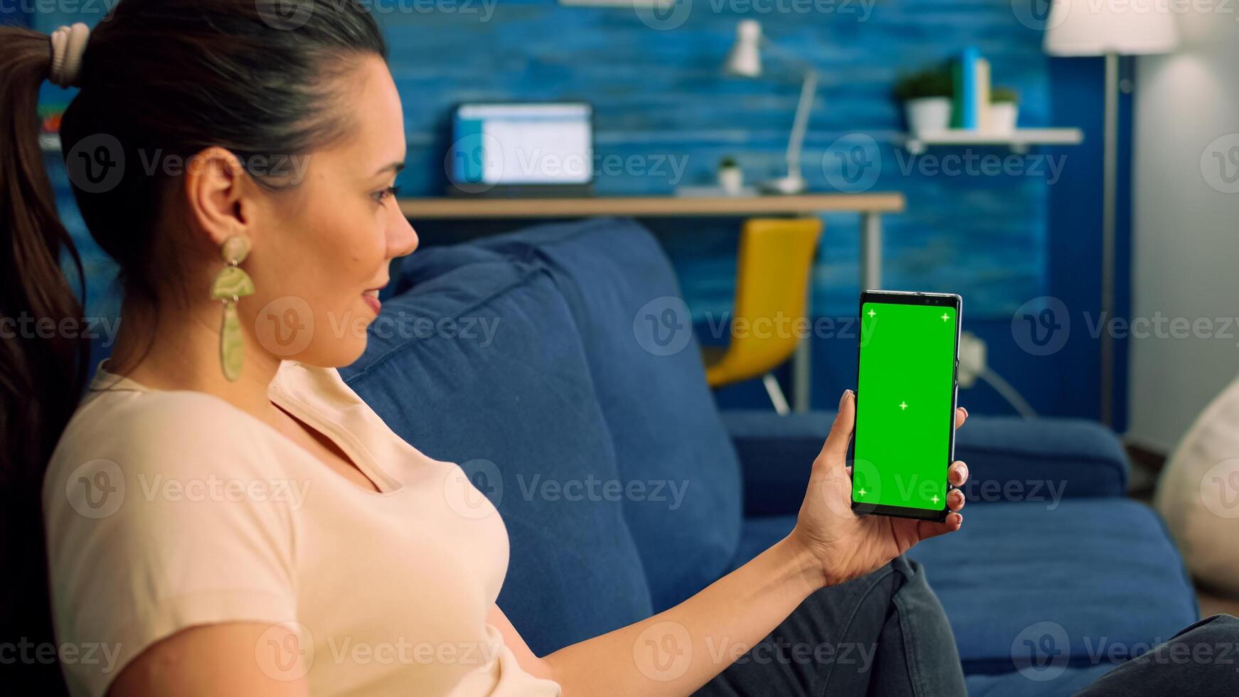 Freelancer woman sitting on sofa in living room, looking at isolated smartphone with mock up green screen chroma key in landscape mode. Caucasian female browsing on internet with friends photo