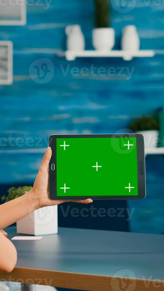 Woman looking at tablet computer with mock up green screen chroma key display browsing on internet searching lifestyle ideas. Freelancer using isolated device standing on desk office in living room photo