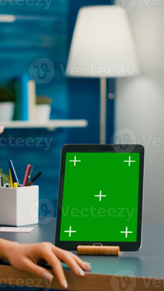 Freelancer woman holding cup of coffee looking at tablet computer with mock up green screen chroma key sitting on desk table. Caucasian female browsing on isolated device from home office room photo