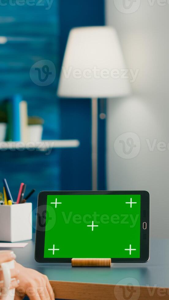 Caucasian female looking at tablet computer with mock up green screen chroma key sitting on office desk in living room. Freelancer woman browsing on social network using isolated device photo