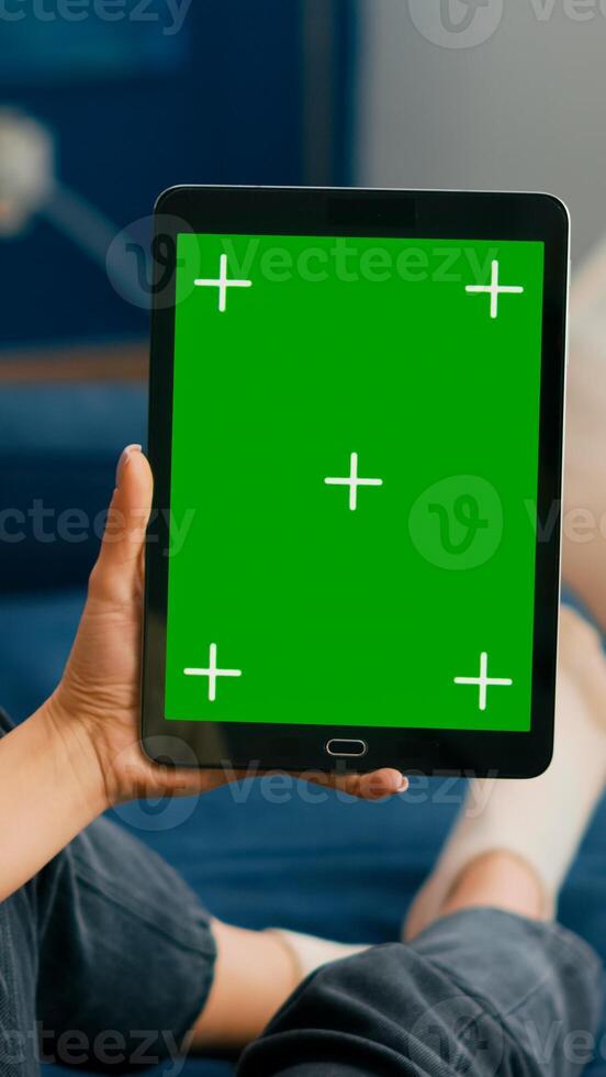 Caucasian female lying on sofa having online meeting on tablet computer with mock up green screen chroma key display. Woman using isolated touchscreen device for social networks browsing photo