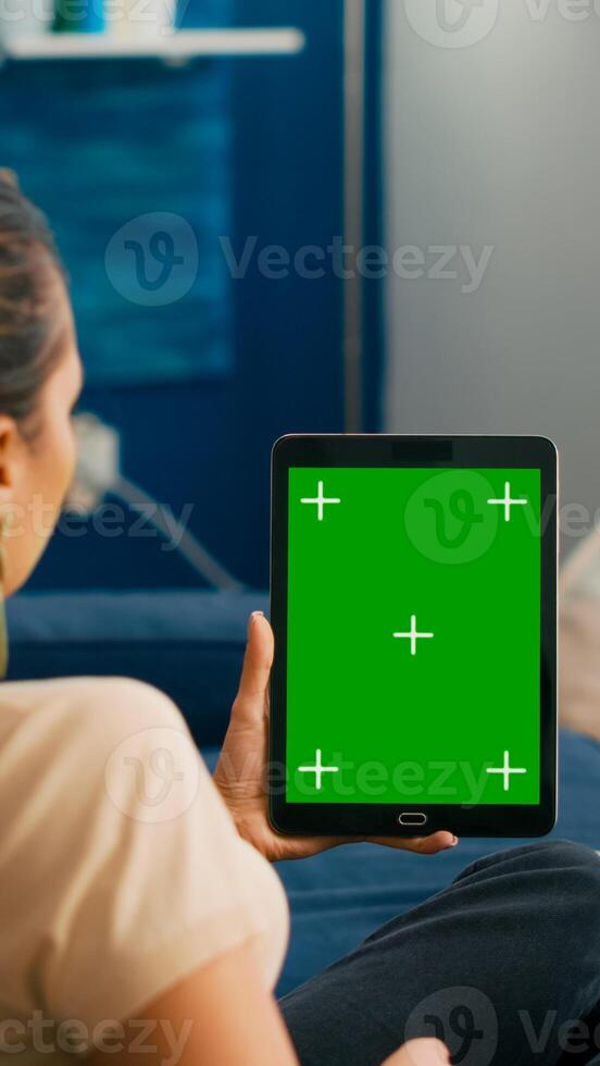 Business woman looking at tablet computer with mock up green screen chroma key display sitting on sofa in living room. Freelancer using isolated touchscreen device for social networks browsing photo