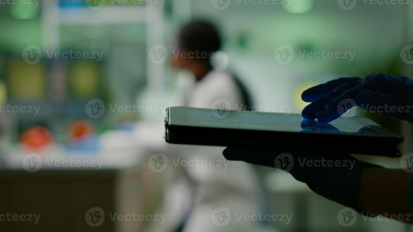 Scientist researcher doctor analyzing genetic mutation test using tablet while her collegue typing biological expertise on computer in background. Medical team working in microbiology laboratory photo