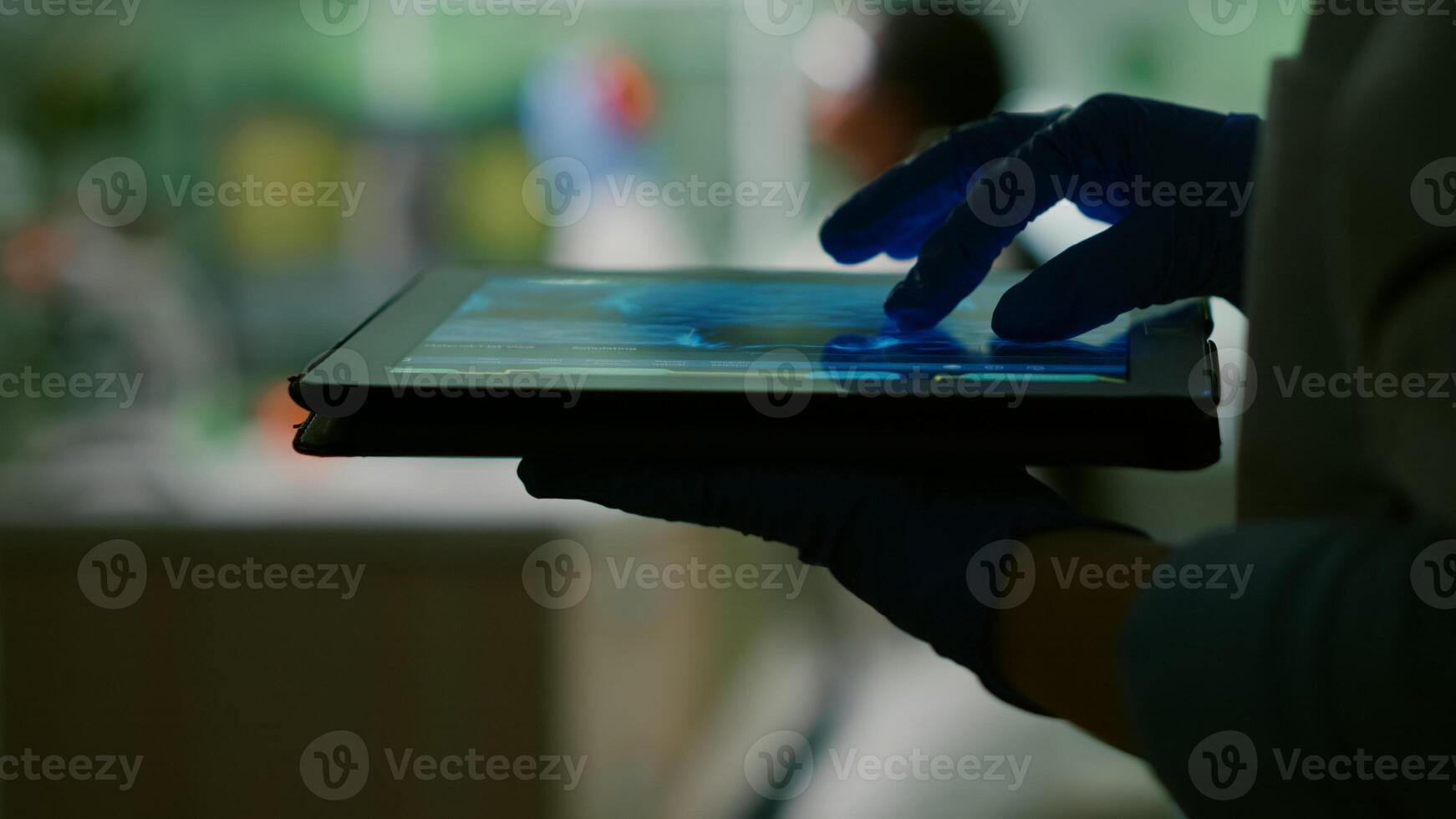 Chemist scientist woman checking dna sample test using tablet while her collegue typing microbiology experiment on computer in background. Medical team working in microbiology laboratory photo