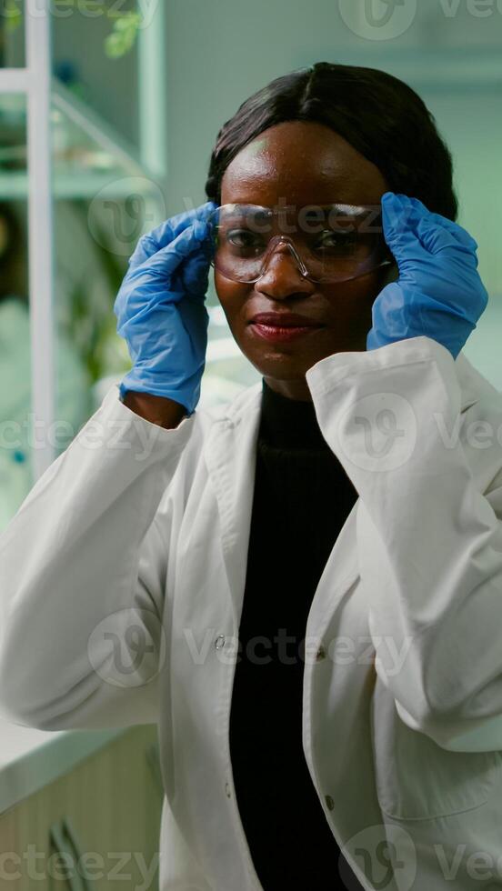 Portrait of african biologist in white coat looking into camera working in microbiology laboratory. Specialists team researching genetic mutation developing dna GMO biology test photo