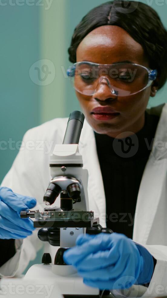 Portrait of pharmaceutical woman putting slide under microscope examining biological sample for medical experiment. Biologist analyzing organic agriculture plants in microbiology scientific laboratory photo