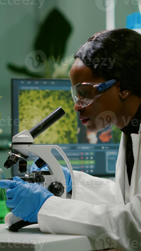 Biologist woman looking at test sample under microscope working at gmo experiment. Pharmaceutical scientist analyzing organic agriculture plants in microbiology scientific laboratory photo