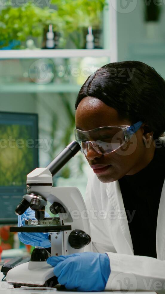Slide view of biologist researcher analyzing gmo green leaf using medical microscope. Chemist scientist examining organic agriculture plants in microbiology scientific laboratory photo