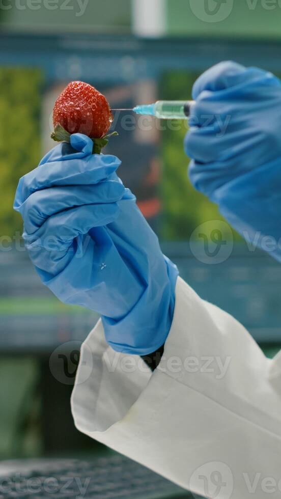 Closeup of biologist scientist injecting strawberry with dna liquid checking fruits for pharmaceutical medical experiment. Biochemist working in farming laboratory testing food for medical expertise photo