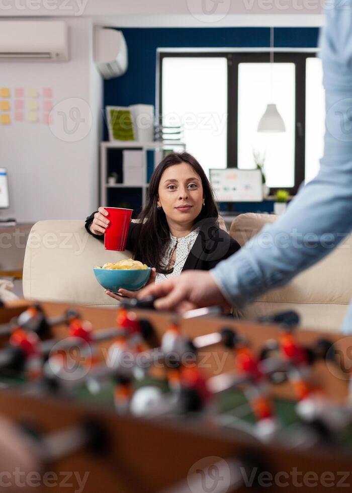 Caucasian woman holding cup of beer and chips after work looking at foosball table soccer game football for fun enjoyment entertainment. Happy worker drinking alcohol at party photo