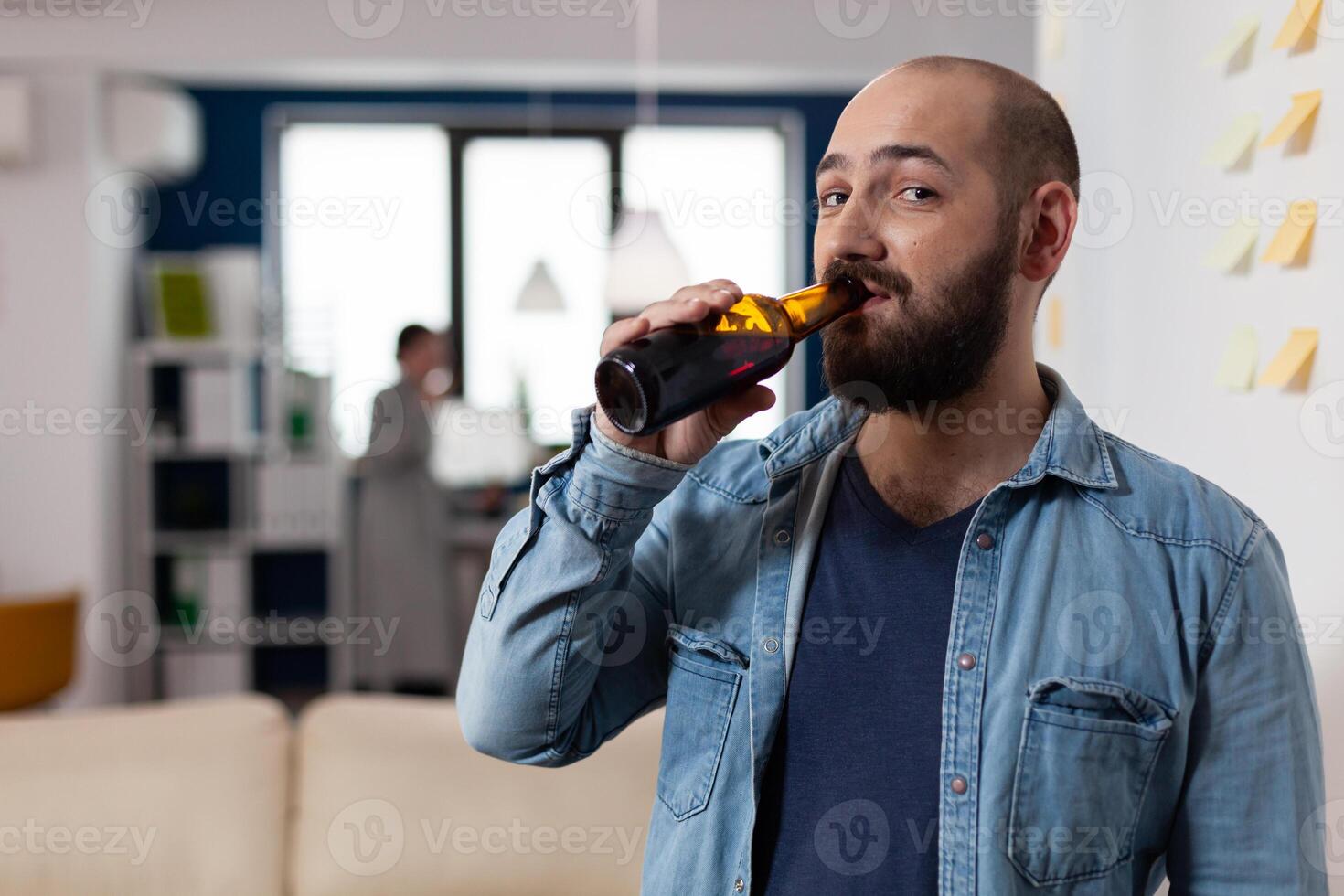 Man drinking bottle of beer after work meeting with colleagues for fun enjoyment. Cheerful celebration with coworkers at office while eating and drinking alcohol. Happy friends partying photo