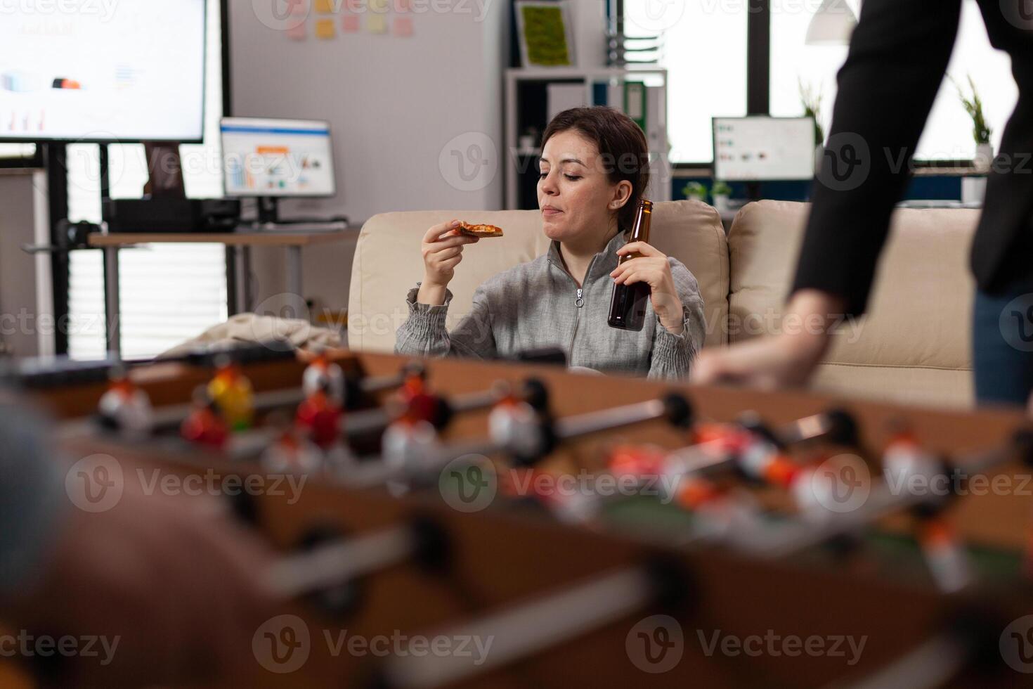 Portrait of cheerful woman eating pizza and drinking beer after work in business office with colleagues. Young person enjoying party celebration after hours, doing fun activity with friends. photo