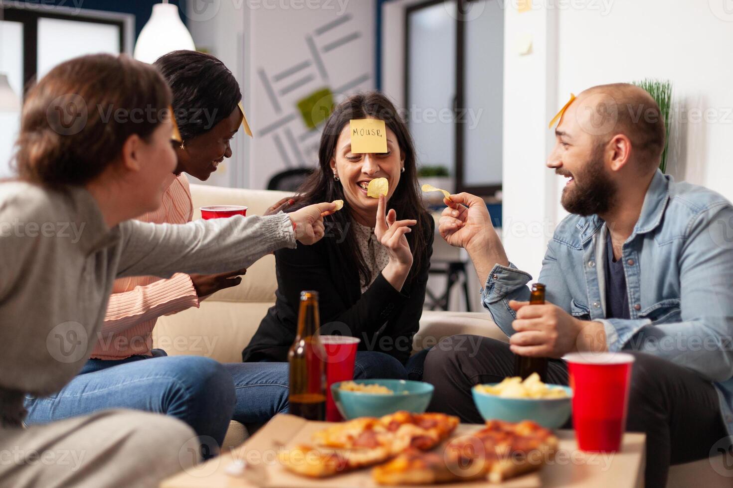 Man and women enjoying guessing game with sticky notes, playing charades together at drinks celebration after work hours. Office workmates having fun with patnomime activity at party. photo