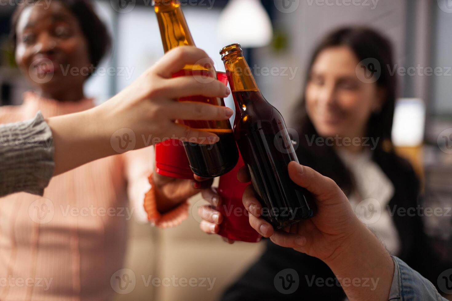 Office colleagues making toast and clinking glasses of alcohol, having drinks after work hours. Cheerful people enjoying champagne, wine or beer, doing cheers symbol at party. Close up. photo