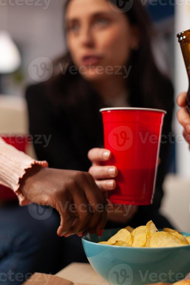 Office workers having fun with alcoholic beverage and chips at after work celebration. Colleagues enjoying beer in bottles and glasses, eating snacks and laughing together after hours. Close up. photo