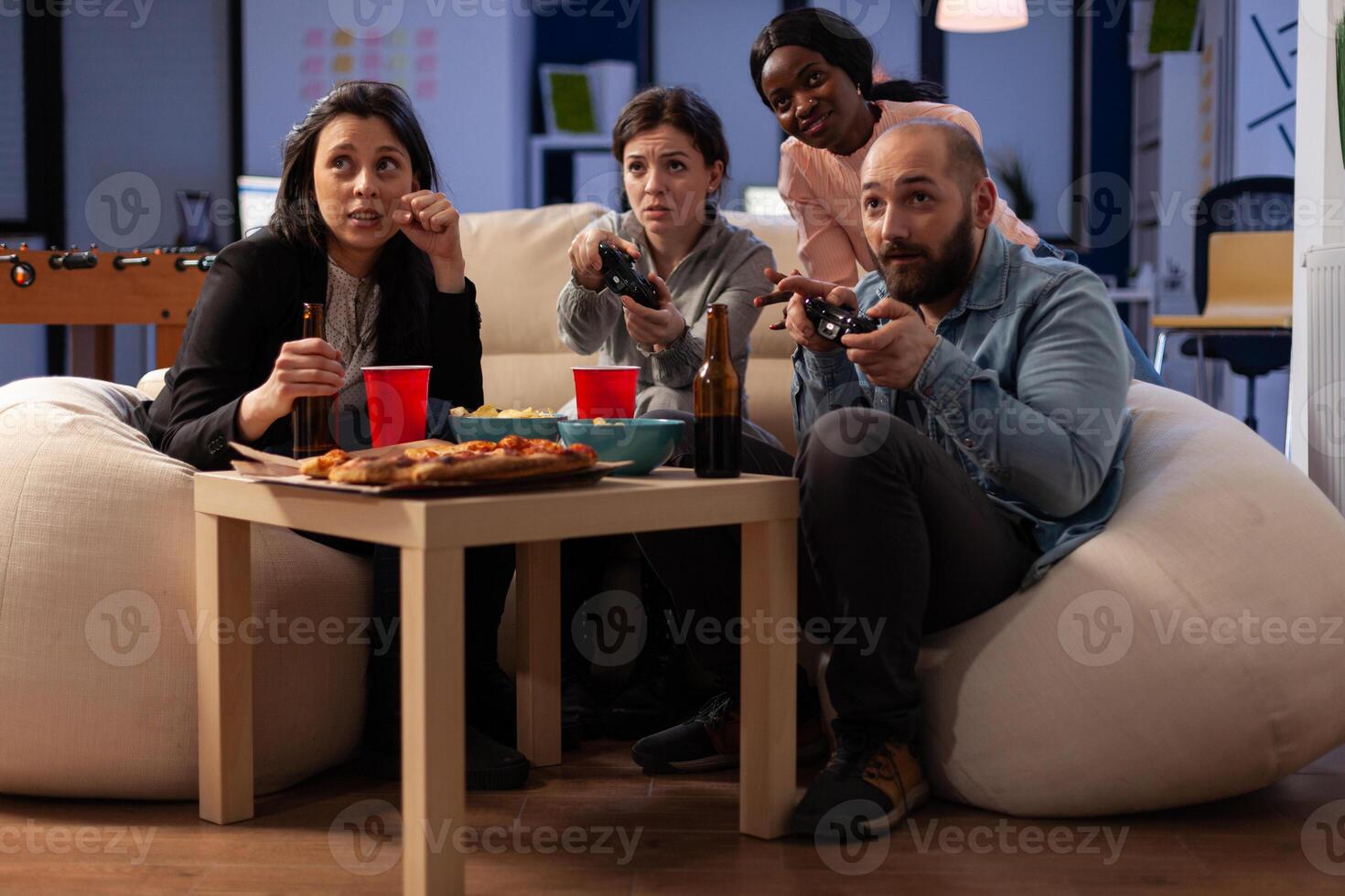 Diverse group of people playing games on console, using controller on tv at office celebration with drinks and food. Colleagues enjoying after work party with alcoholic beverage and game. photo