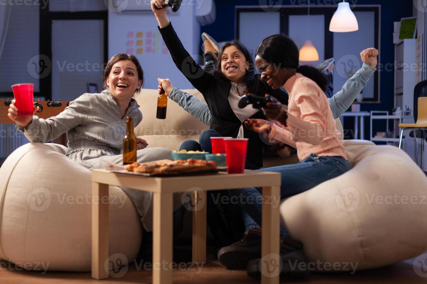 Multiethnic group of people winning games play with joystick on console, meeting in office for drinks after work hours. Man and women celebrating game win and drinking beer. photo