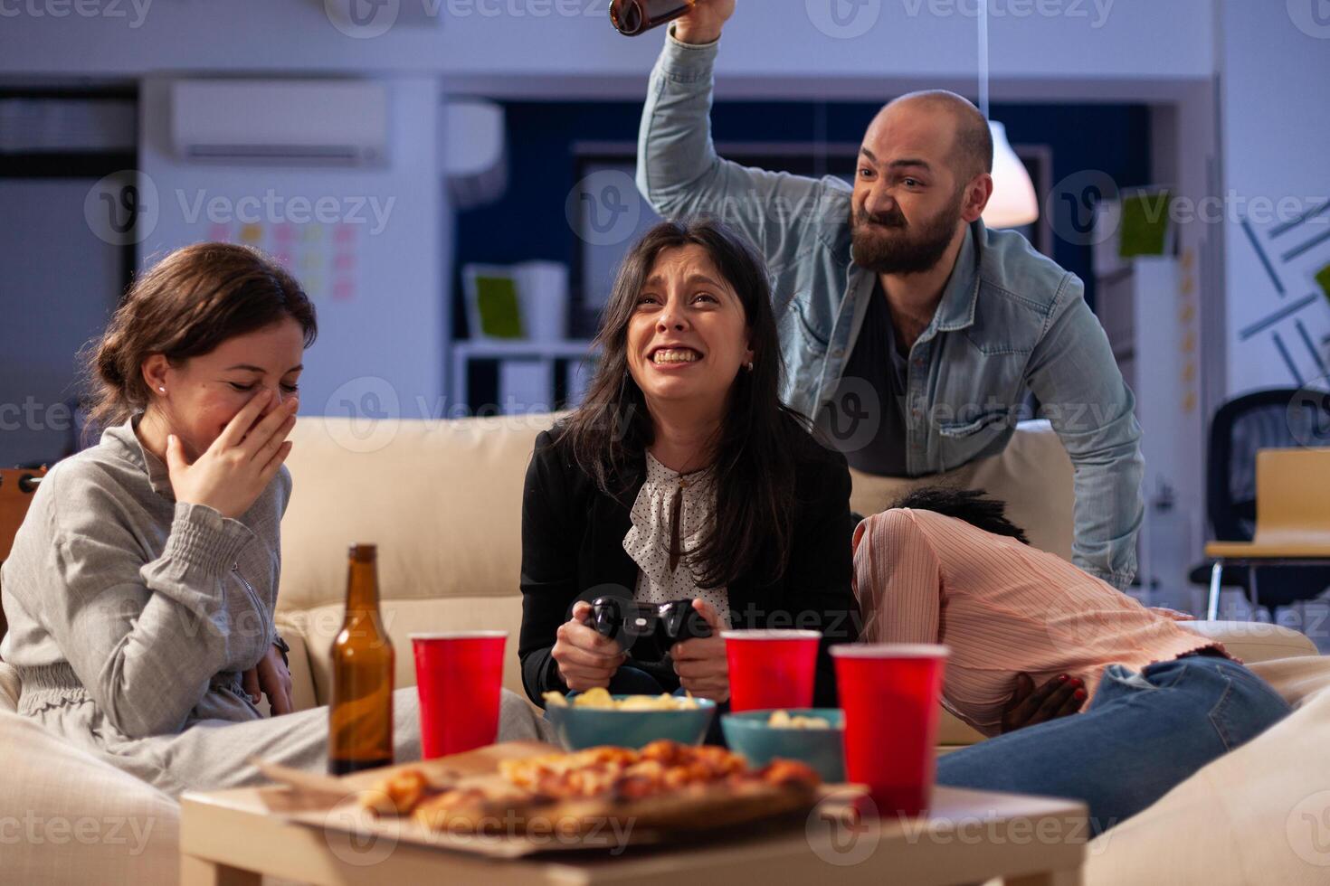 Sad woman losing games play on tv console with controller, attending office party after work hours. Colleagues using online game play at drinks celebration with food snacks. photo