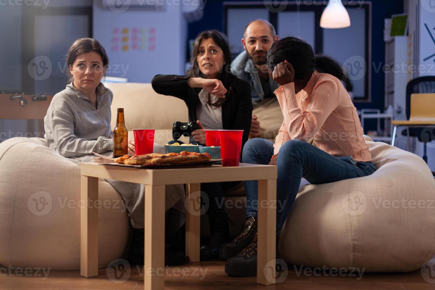 Coworkers feeling frustrated about lost games play, doing leisure activity at office party after hours. Sad colleagues having fun with technology, beer bottles and pizza at celebration. photo