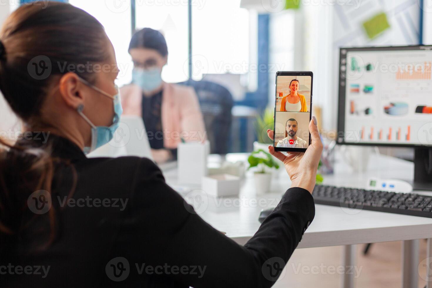 Back view of woman with face mask talking during business call keeping social distancing at workplace, safety precaution against infection with covid19 flu at workplace. photo