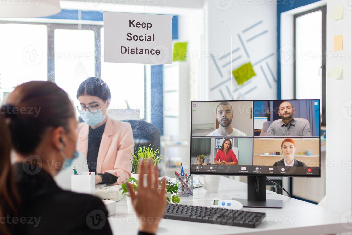Business woman saying hello during remove conference in new normal workplace wearing face mask as safety prevetion during global pandemic with covid10. Keeping social distancing from coworker. photo