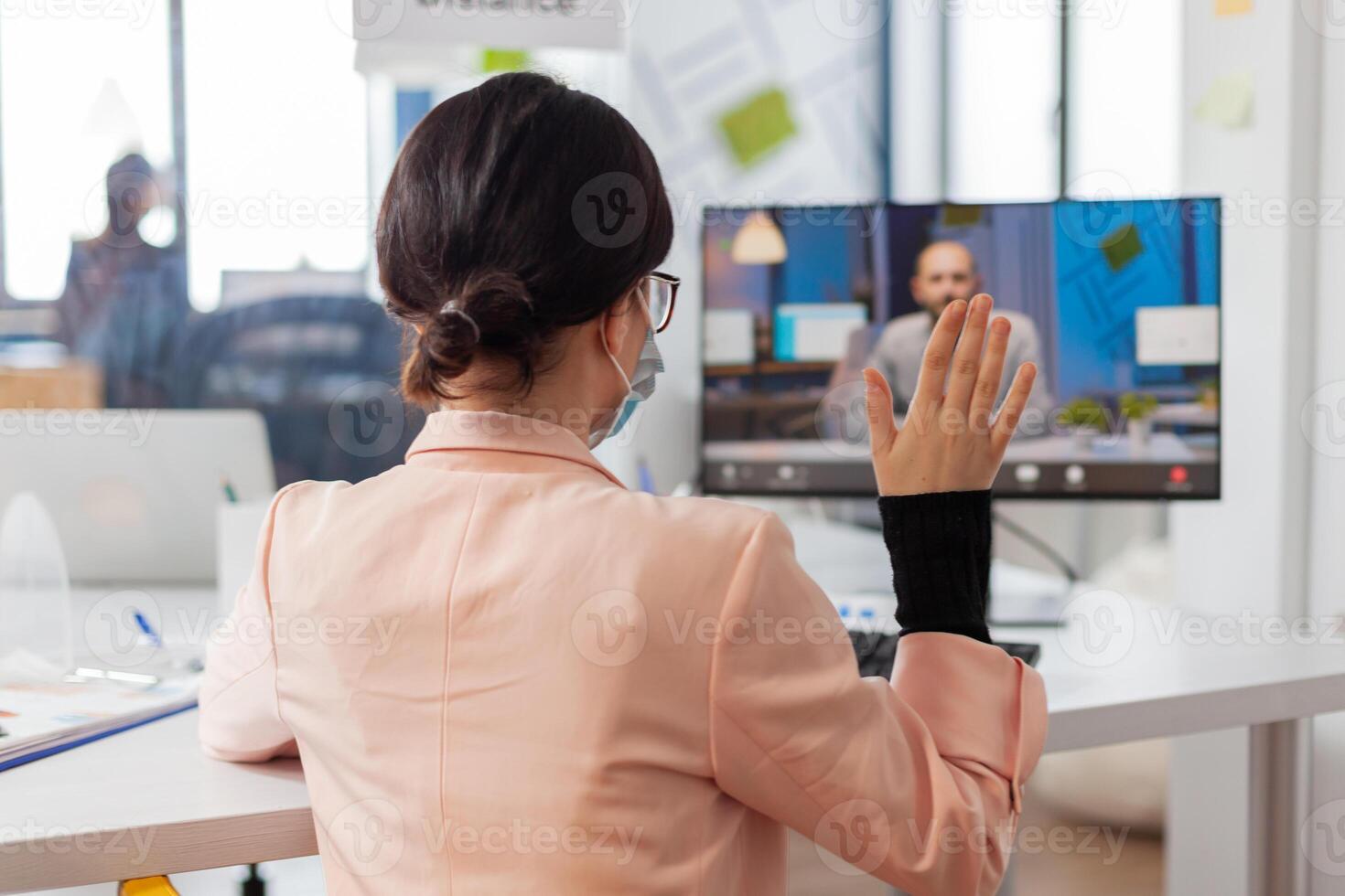 Woman discussing job project with business man during remote call in new normal office in time of global pandemic with covid19, wearing face mask safety prevention against infection. photo