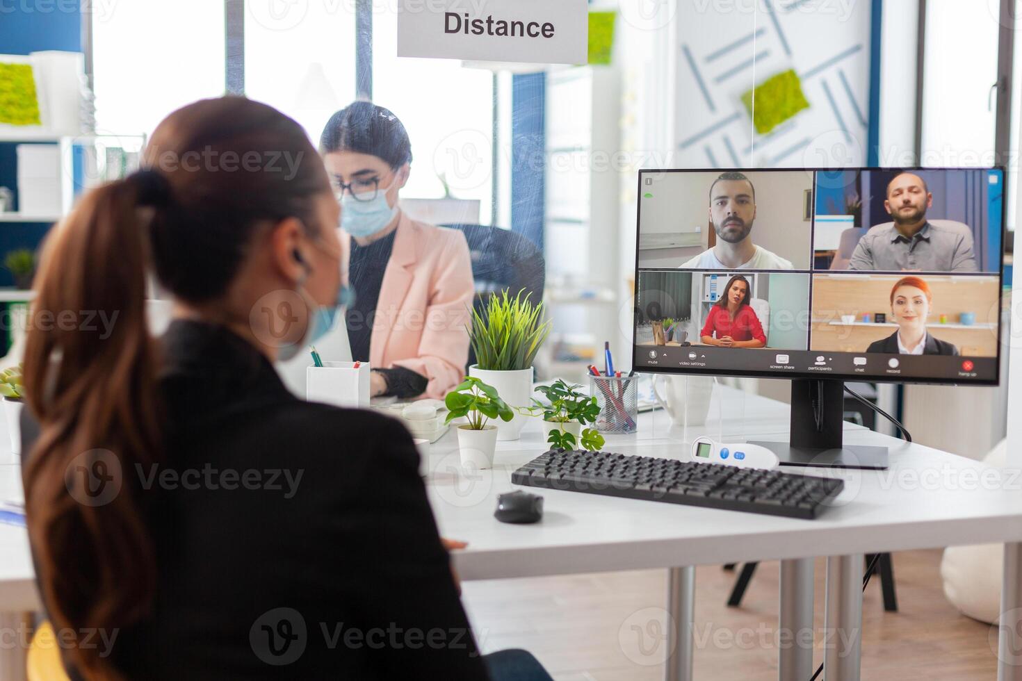 Back view of woman talking with team during remote conference in new normal office in timp of global pandemic with coronavirus, keeping social distancing wearing face mask. photo