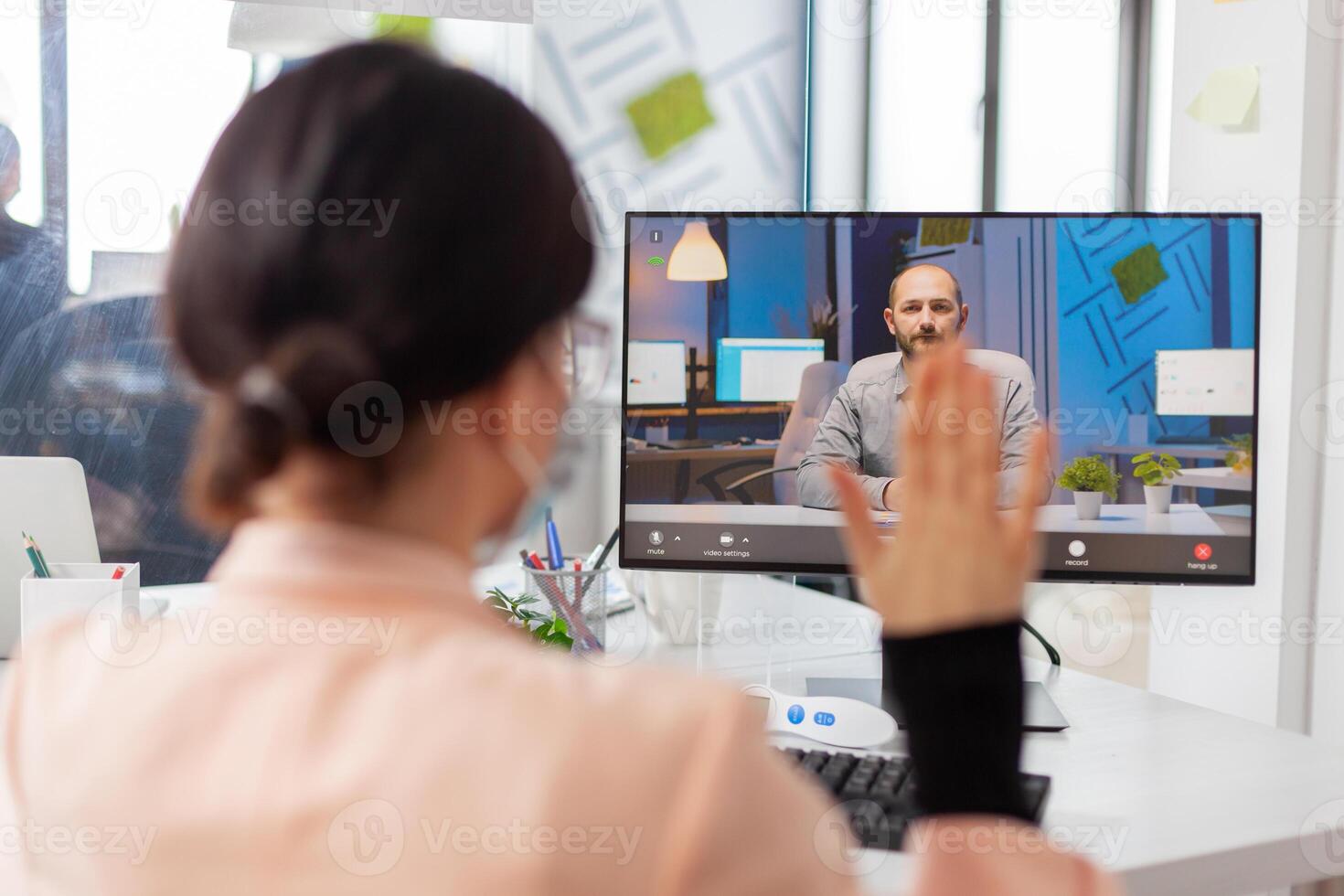 Woman greeting businessman during call from new normal business ofice, in time of covid19 outbreak. Coworkers discussing project on remote call wearing face mask as safety prevention. photo