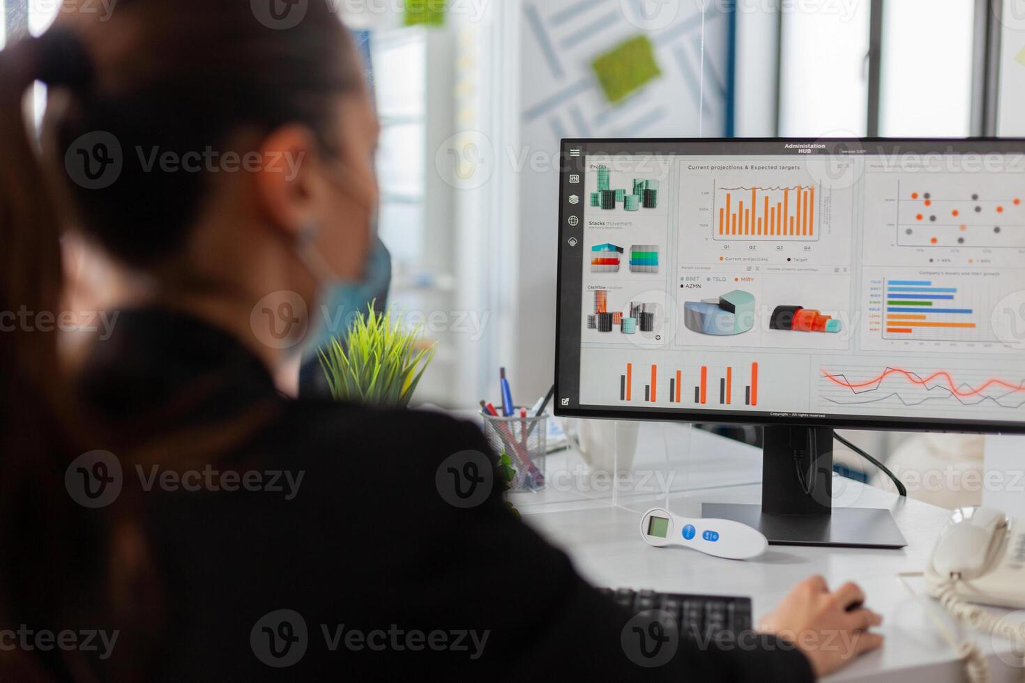Businesswman analysing financial statistics in new normal offfice, wearing face mask as safety prevention during global pandemic with coronavirus flu, keeping social distancing. photo