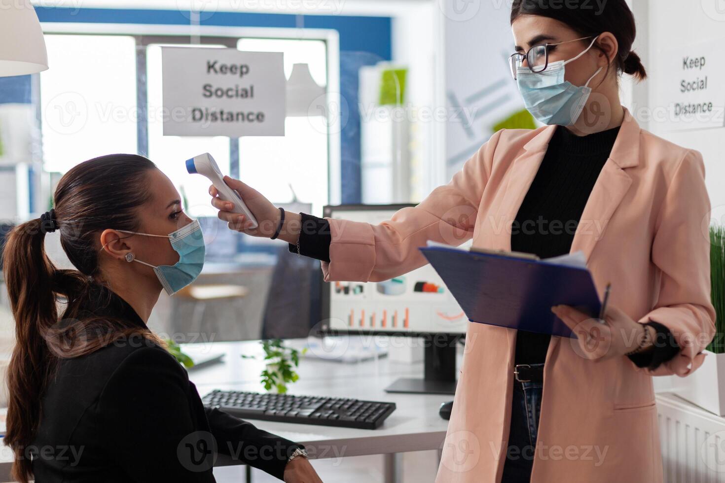 Businesswoman measuring temperature using infrared thermometer to prevent infection with coronavirus. Manager with medical face mask against covid19 working in business office during virus pandemic photo