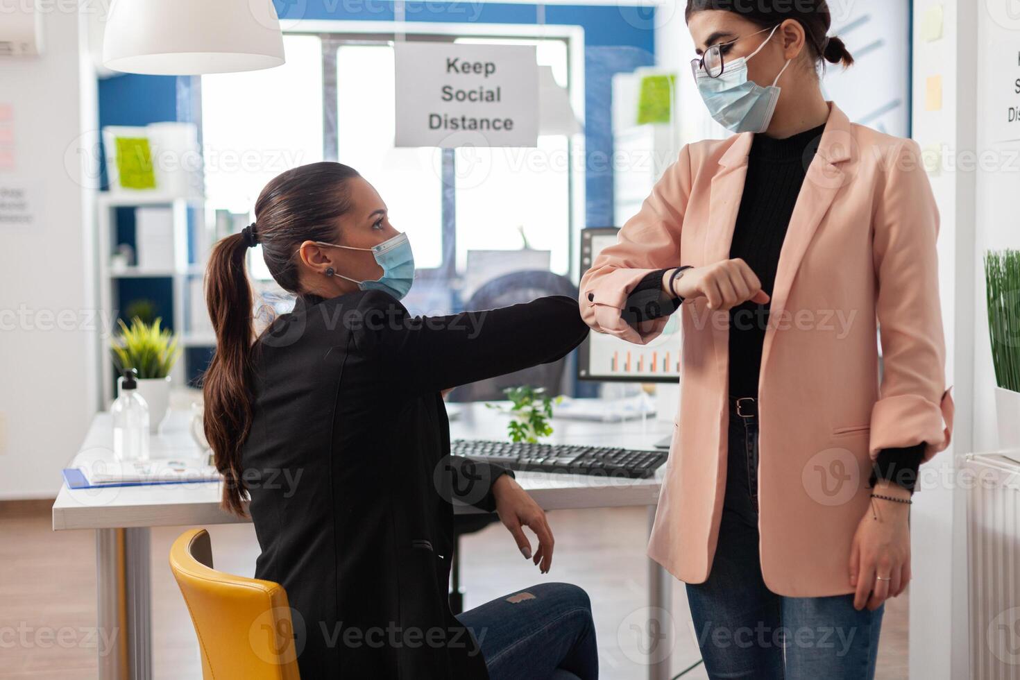 Businesswoman touching elbow with manager to prevent infection with coronavirus during global pandemic. Teamwork with protective medical face masks against covid19 working in startup business office photo