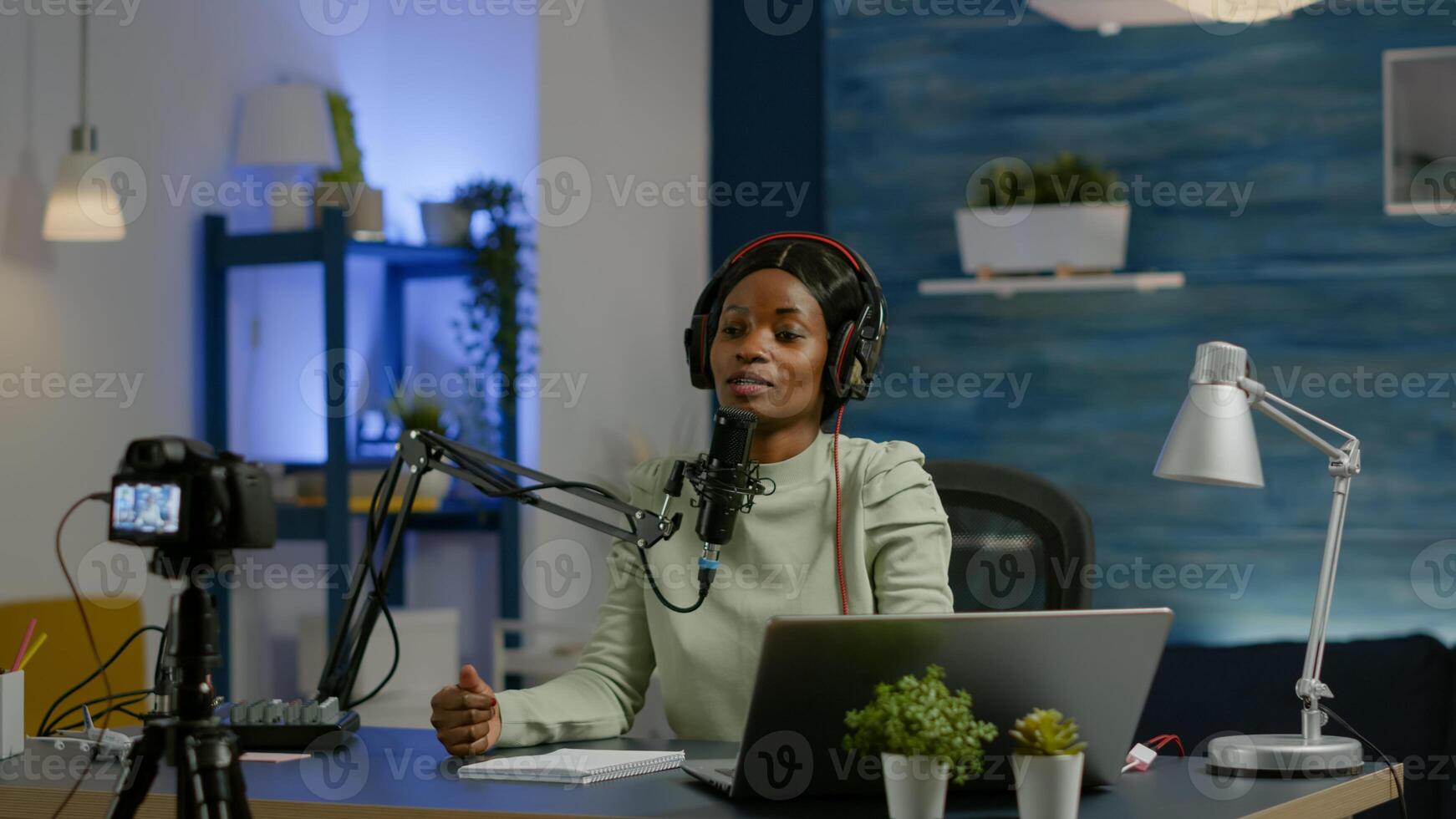 African social media woman looking in laptop talking at microphone recording podcast for youtube channel using camera. Online show On-air production internet broadcast host streaming live photo