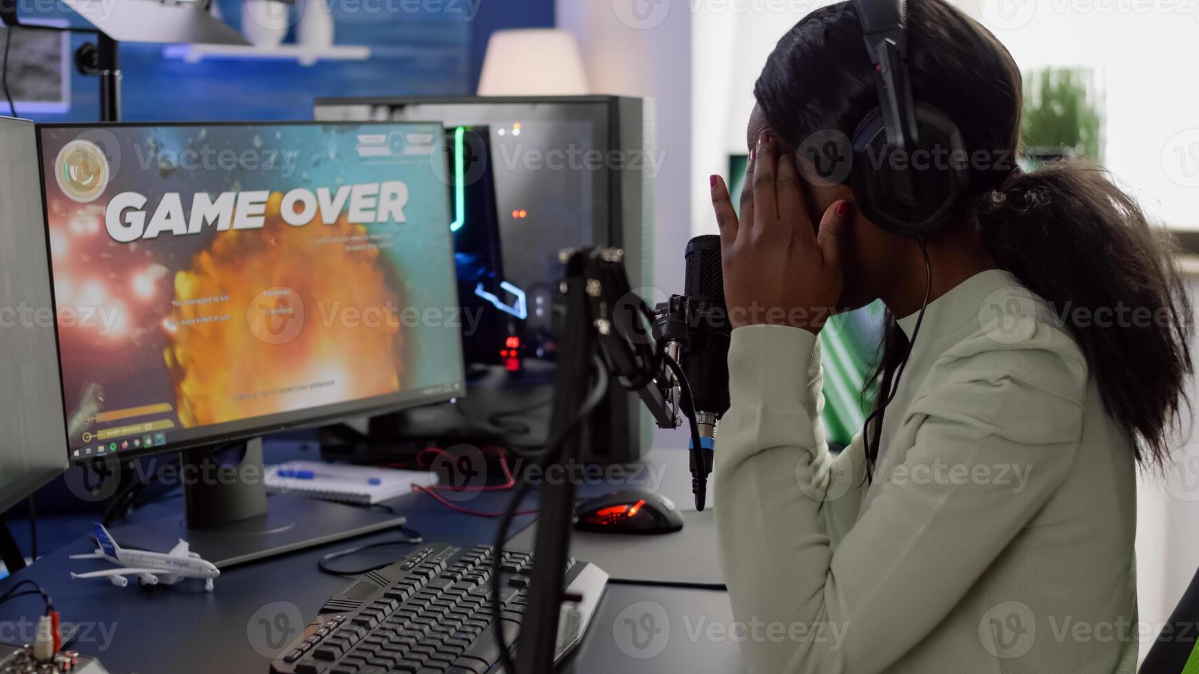 Furious black woman gamer with headphones using stream chat losing game playing on RGB powerful computer shooter game. Virtual online streaming cyber checking sound performing in gaming tournament photo