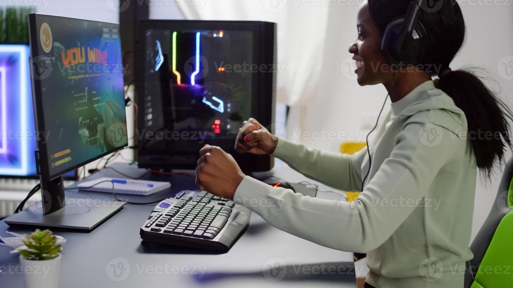 Happy black gamer raising hands winning space shooter online competition talking at professional microphone in gaming studio. Gamer playing online game with streaming chat open during tournament photo