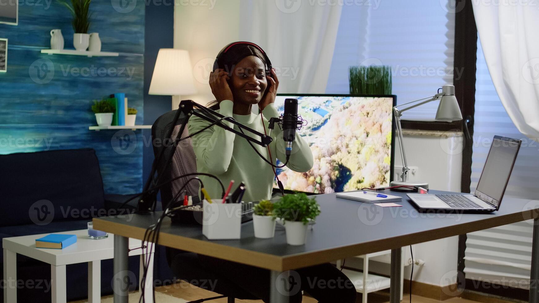 African blogger influencer putting on headset and smiling before recording blog, looking at camera. Social media content creator speaking during livestreaming, blogger discussing in podcast photo