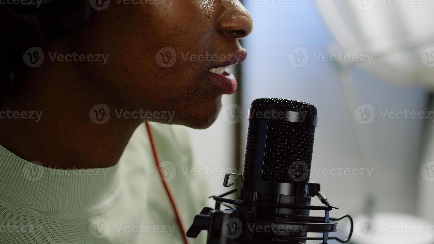 Close up of afro woman vlogger making new blog in home studio talking in professional microphone with audience. Speaking during livestreaming, blogger discussing in podcast wearing headphones. photo