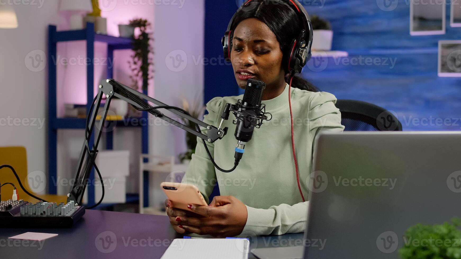 African vlogger recording blog reading messages from smartphone with modern equipment in studio podcast. Influencer looking at phone talking in broadcast using tech to connect with audiences photo
