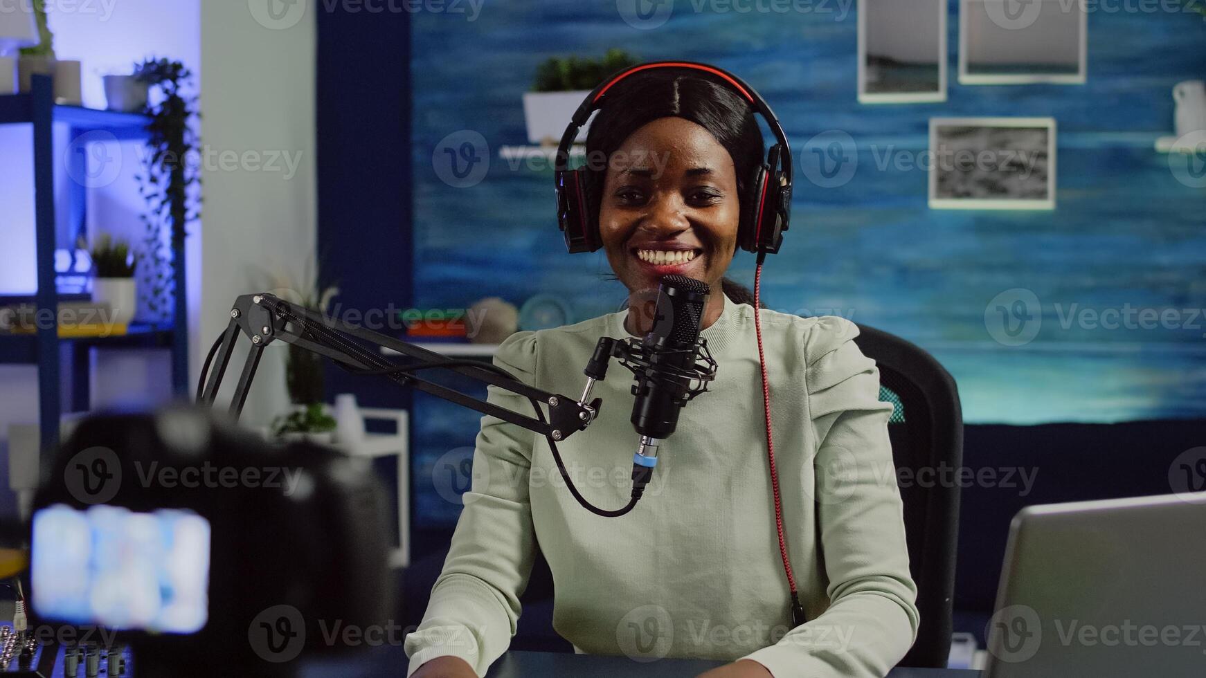 Close up of camera recording african influencer talking looking into it during online podcast. Social media content creator streaming online broadcast, blogger discussing wearing headphones. photo
